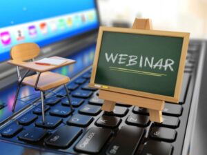 Webinars Image = Mini chair and Mini blackboard sat on a computer keyboard. On the blackboard it says "Webinar"